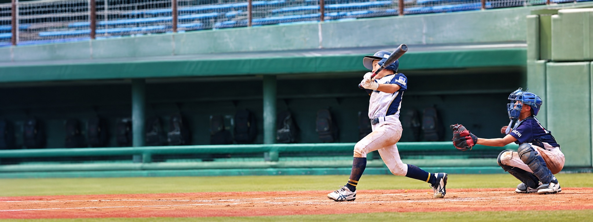 全国大会の球場で力強くスイングする少年野球選手と捕手